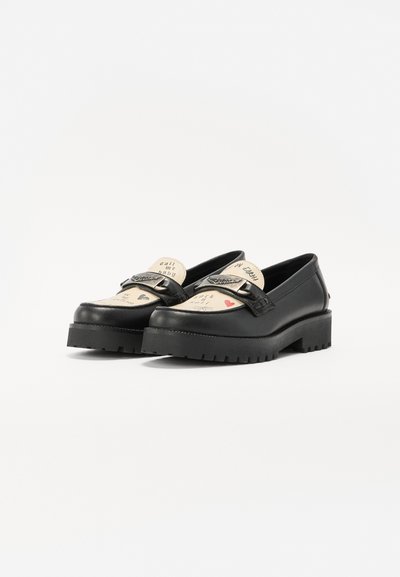 Black slip-on shoes featuring a beige design with printed text and heart motifs, a chunky rubber sole, and a decorative strap with hardware.