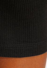 Črna rebrasta tkanina z gladko teksturo, s prišitimi šivi na robu. Prikaz v bližnjem posnetku poudarja vzorec in gosto tkanje materiala.