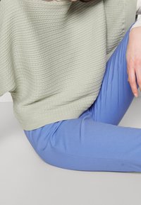 Ljusgrön texturerad stickad tröja i kombination med figursydda pastellblå byxor. Tröjan har horisontell ribbning som skapar ett upphöjt mönster.