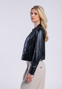 Czarna skórzana kurtka bomberka z zamkiem z przodu, dopasowany fason i gładka faktura. Posiada boczne kieszenie i skróconą sylwetkę.