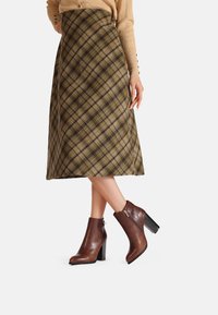 Stivali ankle in pelle marrone con finitura testurizzata e tacco a blocco, abbinati a una gonna a quadri nei toni oliva, marrone e beige.