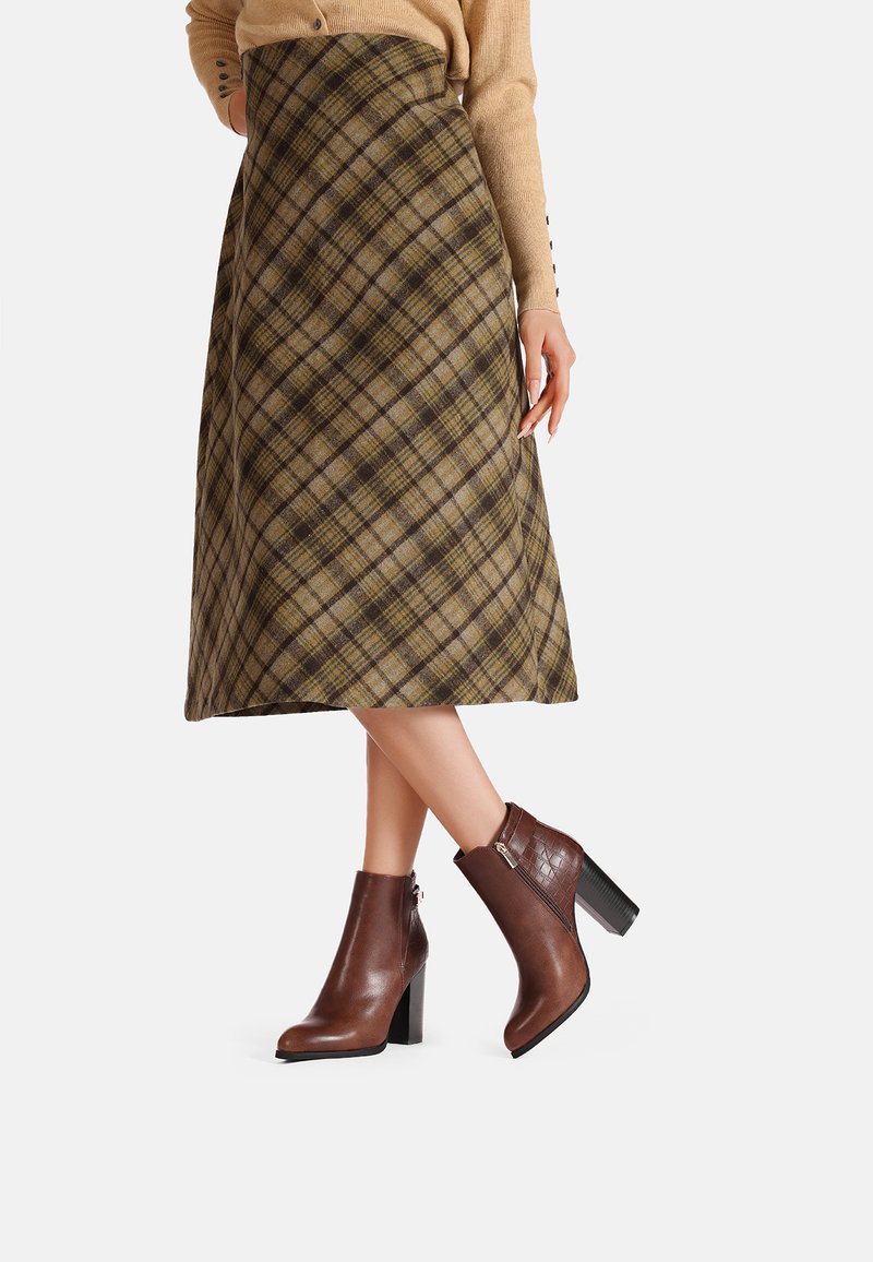 Stivali ankle in pelle marrone con finitura testurizzata e tacco a blocco, abbinati a una gonna a quadri nei toni oliva, marrone e beige.