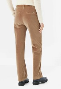 Bruna kordflorbyxor med rak ben-design, bakfickor och svarta ankelstövlar. Slät textur, avslappnad stil och skräddarsydd passform.