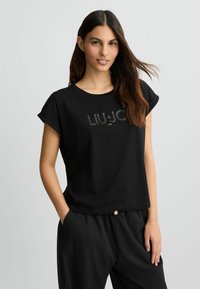 T-shirt nera a maniche corte realizzata in tessuto morbido, con un logo 'LIU·JO' in finitura lucida ben visibile sul petto. Vestibilità rilassata.