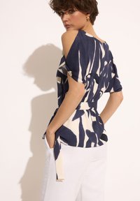 Błękitna i kremowa bluzka w wzory z odkrytymi ramionami, z paskiem w talii i luźnym krojem, wykonana z lekkiego materiału.