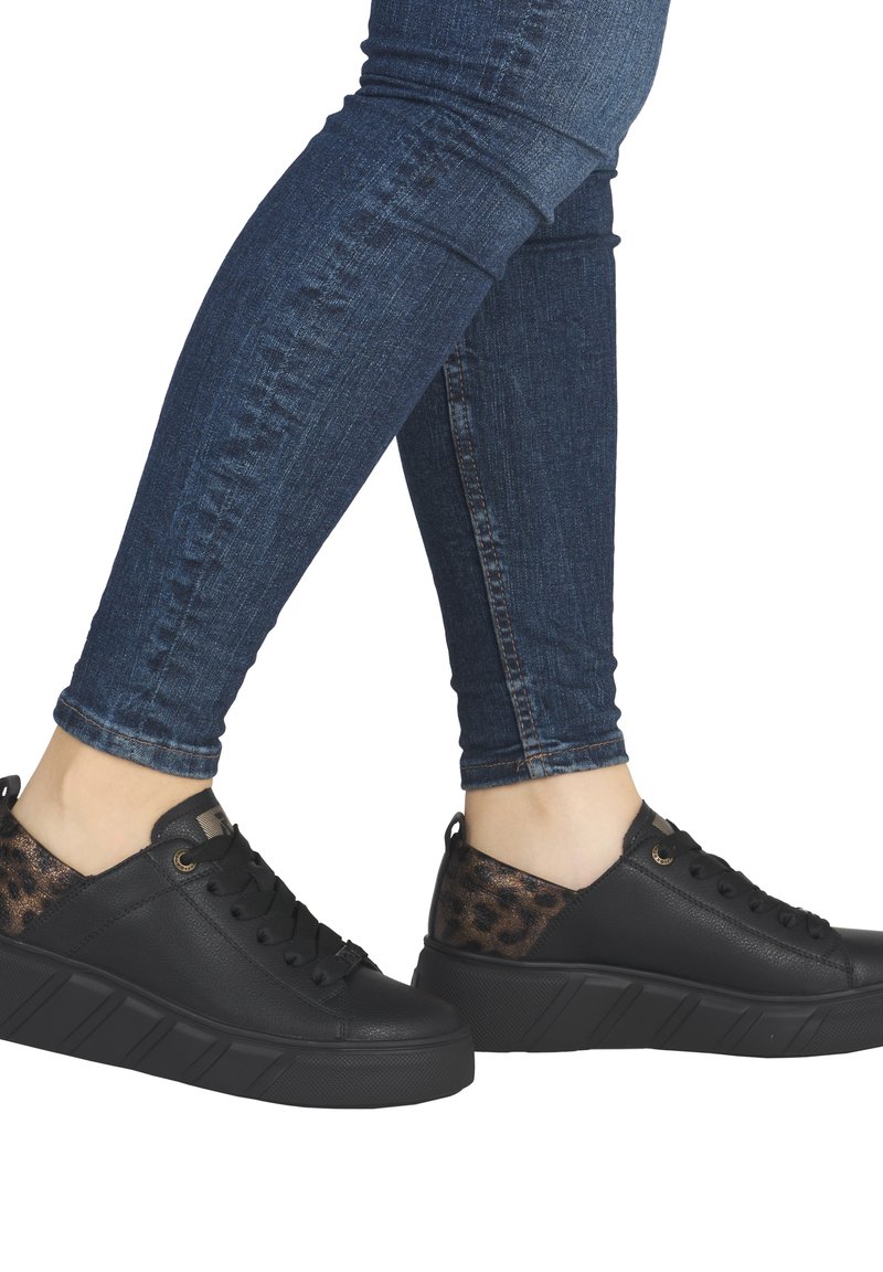 Baskets en cuir noir avec un accent en imprimé animal texturé, semelle plateforme et six œillets, accompagnées d'un jean skinny bleu foncé.