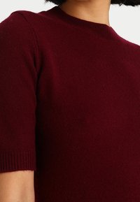 Burgundin lyhythihainen neulepaita pyöreällä kaula-aukolla, jossa on pehmeä textura ja ribbireunat tiiviiseen istuvuuteen.