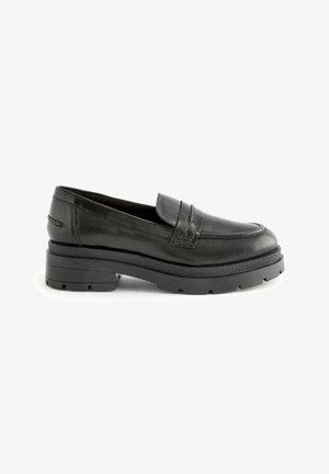 Mocasines de cuero negro con punta redondeada, detalles de costura y una suela gruesa y texturada en negro. Diseñados con un clásico acento de tira tipo penny.