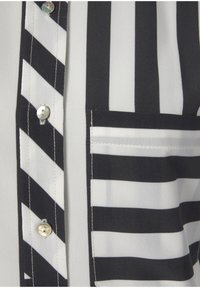Camicia a righe in bianco e nero con linee verticali e diagonali, chiusura con bottoni simili a perle e taschino a toppa.
