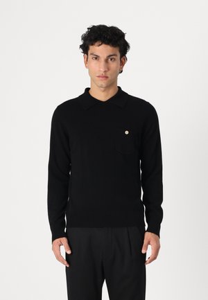 Schwarzer gestrickter Polopullover mit Kragen, ausgestattet mit einer kleinen Fronttasche und einem goldfarbenen Akzentknopf, auf einem Modell vor einem schlichten Hintergrund präsentiert.