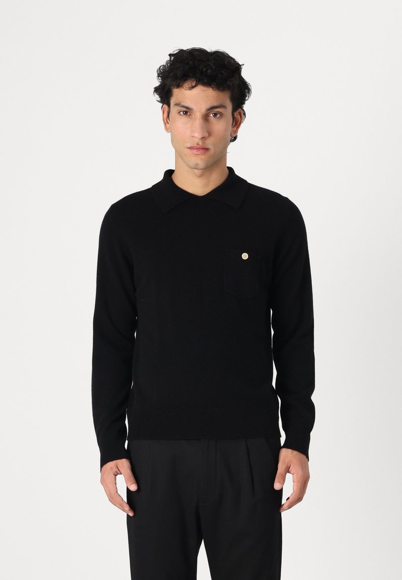 Maglione polo lavorato a maglia nero con colletto, dotato di una piccola tasca frontale e di un bottone dorato, indossato da un modello su uno sfondo neutro.