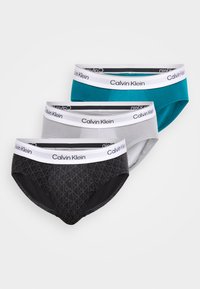 Tri páry nohavičiek Calvin Klein v čiernej farbe s vzorom, sivej a tyrkysovej. Všetky majú biely elastický pás so logom.