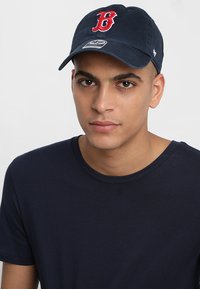Navy blue cotton cap featuring a raised red "B" logo on the front, with a curved brim and an adjustable strap at the back.