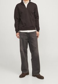 Sudadera de cremallera marrón oscuro sobre una camisa blanca de cuello, combinada con jeans de mezclilla gris holgados y zapatos de cuero marrón oscuro.