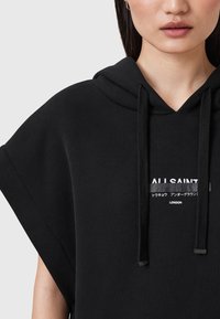 Svart hoodie med oversized ärmar, dragsko i huvan och logotypdetalj fram i vitt. Tillverkad av ett mjukt tyg med en slät yta.