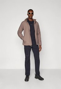 Heledat beežikas jakk kapuutsiga, kandes seda tumeda särgi peal, tumedad püksid. Mustad jalanõud. Päikeseprillid lisavad moodsat ja minimalistlikku hõngu.