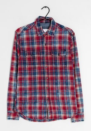 Long-sleeve red, blue, and white plaid button-up shirt with two chest pockets hanging on black hanger against white background.