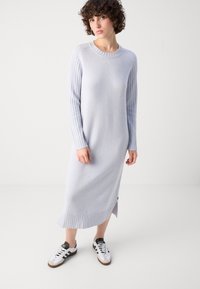 Lys grå, kne-lengde genserkjole med ribbede ermer og kant. Laget av mykt materiale, med en sidesplit og rund hals.