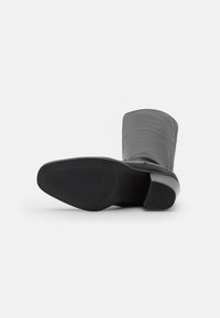 Botte noire en cuir montant jusqu'au genou avec un bout arrondi et un petit talon bloc. La semelle présente du caoutchouc texturé pour une meilleure adhérence. Fini lisse et sans ornement.