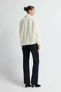 Crème blouse met een kraag, relaxte pasvorm, lange mouwen, gecombineerd met donkere denim rechtlopende broek en zwarte enkellaarsjes met hak.