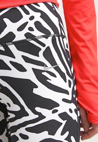 Leggings a fantasia bianca e nera con un materiale liscio e elastico, con cuciture in contrasto e un piccolo logo Nike argento.