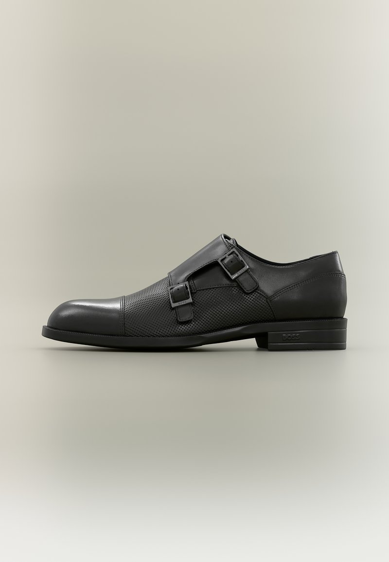 Czarne skórzane męskie półbuty typu double monk strap z fakturowanym śródstopiem i wypolerowanym czubkiem, płaską podeszwą oraz tłoczonym logo marki na pięcie.