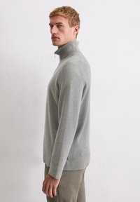 Sweter typu pulower w jasnoszarym kolorze, wykonany z miękkiego materiału. Posiada wysoki kołnierz oraz długie rękawy z delikatnym bocznym rozcięciem u dołu.