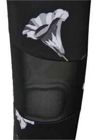 Sorte treningsleggings med et blomsterdesign i grå og hvite farger, kombinert med mesh-paneler for å gi pusteegenskaper ved kneregionen.