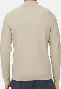 Beżowy sweter z prążkowanego dzianiny z kołnierzem stójkowym, długimi rękawami i dopasowanym dołem; minimalistyczny design bez widocznych logo czy wzorów.