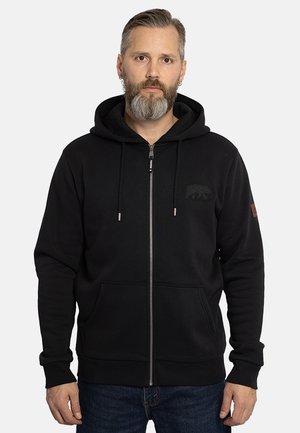 Sudadera con cremallera negra hecha de tejido texturizado. Presenta un bolsillo frontal, capucha con cordón y un logo sutil en el pecho.