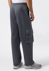 Graue Jogginghose mit lockerem Schnitt, elastischem Bund, Seitentaschen und einer großen Cargo-Tasche am linken Bein. Glatte Stofftextur.