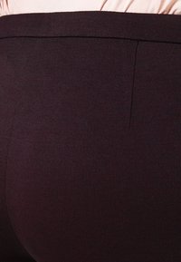 Tmavě burgundová přiléhavá část oděvu s hladkým, texturovaným povrchem. Obsahuje čistý pas a jemný detail sklady.