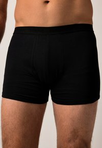 Boxers noirs ajustés avec une taille élastique douce arborant le logo. Tissu lisse, longueur mi-cuisse, sans motifs ni accents visibles.