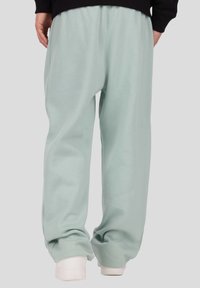 Világoszöld, laza szabású melegítőnadrág elasztikus derék- és szegélypánttal, puha anyagból készült, fehér cipővel párosítva.