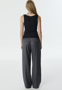 Zwarte mouwloze top met geplooide details, gecombineerd met hooggewaisted grijze wijde broek met twee achterzakken en een gladde textuur.