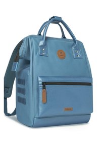 Zaino blu di tessuto con doppi manici superiori, spallacci regolabili, una tasca anteriore con zip e dettagli in pelle. Presenta un logo circolare.