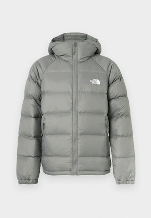 Giacca a vento grigia con cappuccio, caratterizzata da chiusura con zip e polsini a costine. Il materiale ha una texture liscia con una leggera lucentezza. Logo sul petto.