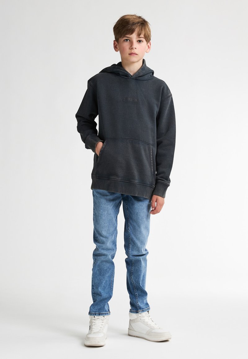 Donkergrijze hoodie met een voorzak, ribbels aan de mouwen en onderkant; gecombineerd met lichtblauwe jeans en witte sneakers. Glad materiaal, casual ontwerp.
