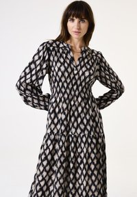 Robe longue à motifs noir et blanc avec un décolleté en V, des manches bouffantes et une taille élastiquée, présentant une jupe à volants.