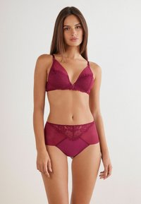 Bordeaux lingerie set met een met kant afgewerkte bralette met verstelbare schouderbandjes en hooggezette slips met kantdetails. Zachte textuur.