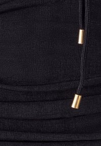 Black ribbed fabric detail with gathered texture; features gold-tone metal accents on drawstring ends. Smooth, soft material.