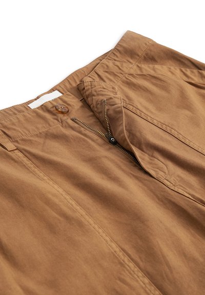 Pantalon marron avec fermeture éclair partiellement ouverte et bouton marron à la taille, montrant la texture du tissu et les détails de la couture.