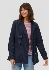 Navyblaue doppelte Jacke mit breitem Kragen, großen Knöpfen und lockerer Passform, die über einem mehrfarbigen Pullover getragen wird. Weicher Stoff.