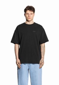 Czarny, oversize t-shirt z bawełny, z okrągłym dekoltem i krótkimi rękawami. Subtelny detal z logo z przodu, w zestawie z jasnoniebieskimi dżinsami.