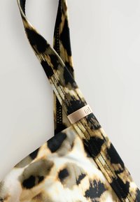 BH mit Leopardenmuster in verschiedenen Brauntönen und Schwarz. Verfügt über gekreuzte Träger und ein metallisches Detail mit eingeprägtem Logo. Glatte Stofftextur.