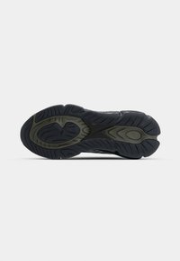 Semelle de chaussure de sport noire et gris foncé avec des empreintes texturées et une bonne adhérence sur fond blanc.