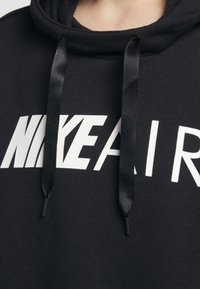 Svart hoodie med en stor vit "NIKE AIR" logga, med svarta dragsnören och en mjuk tygtextur.
