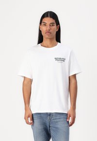 White cotton t-shirt with a round neck and short sleeves. Features green text "REPUBLIQUE FRANÇAISE" on the left chest area.