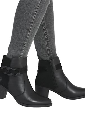 Bottines noires à cheville avec une finition en cuir lisse, dotées d'une sangle tressée, d'une fermeture éclair sur le côté et d'un talon empilé. Portées avec un jean skinny gris.