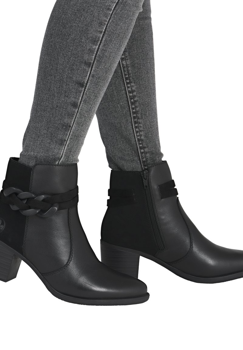 Bottines noires à cheville avec une finition en cuir lisse, dotées d'une sangle tressée, d'une fermeture éclair sur le côté et d'un talon empilé. Portées avec un jean skinny gris.